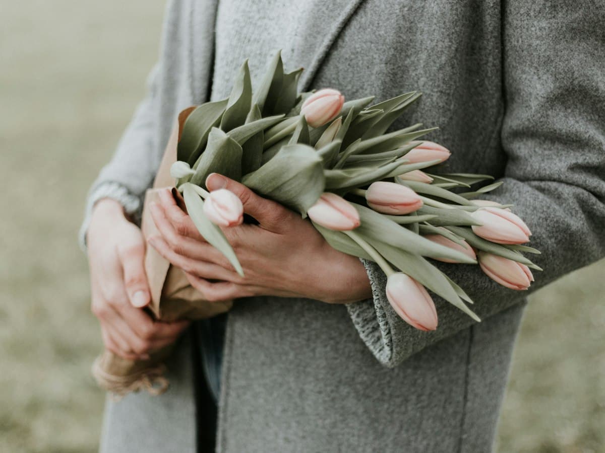 Mains tenant contre soi un bouquet de tulipes rose poudré.